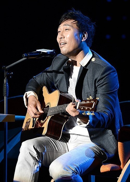 이문세가-의자에-앉아-기타를-치며-노래를-부르는-사진