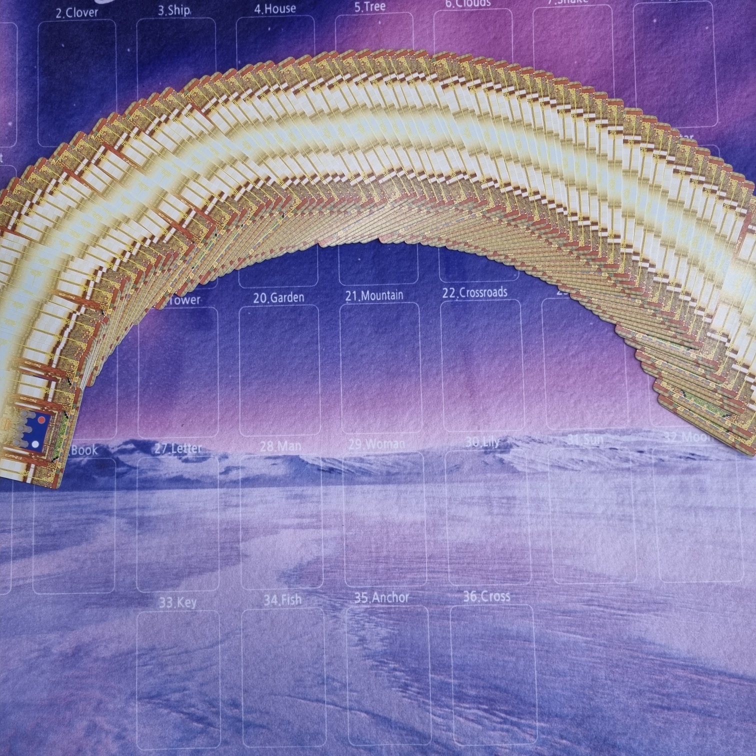 펼쳐진 타로카드 더미 위에 다양한 카드 위치가 인쇄된 매트가 깔려 있다. 배경은 보랏빛 하늘과 눈 덮인 풍경이다.