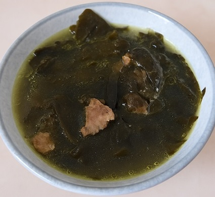 미역국이 연 하늘색 테두리가 있는 그릇에 담겨있다. 국물에 미역과 소고기가 들어 있고 약간의 고기 기름이 떠 있는 소고기미역국.