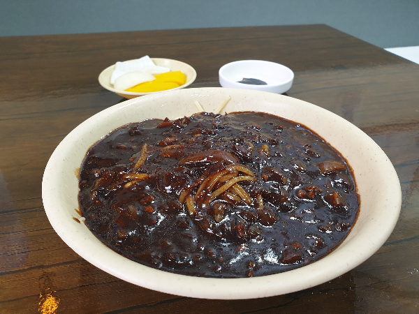 우드 테이블 위에 짜장면과 단문지, 양파 그리고 춘장이 놓여 있다.