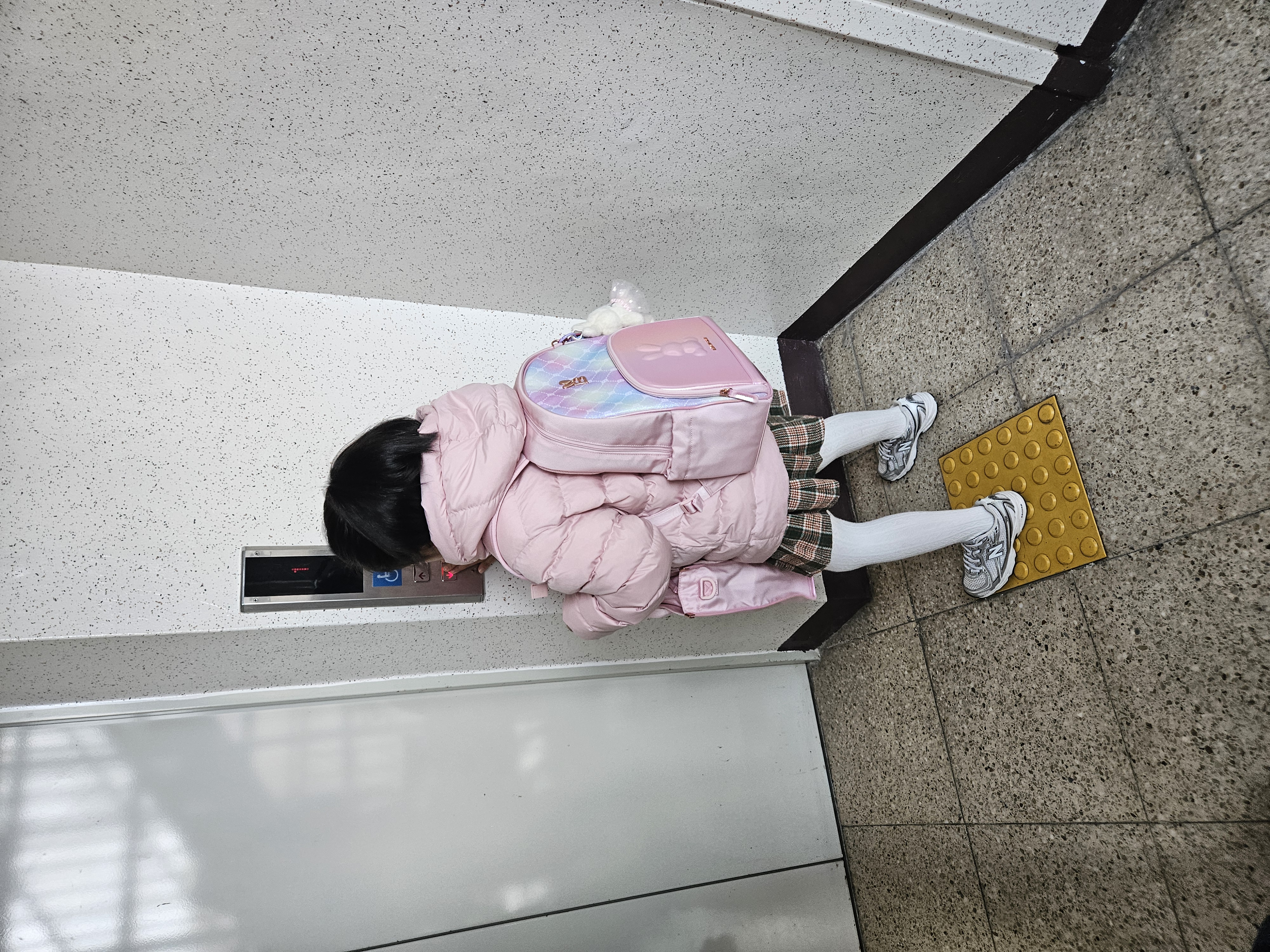 초등학교 입학식 날 아침, 몸집만 한 커다란 새 책가방을 메고 학교에 가기 위해 엘리베이터 앞에서 기다리고 있는 아이의 뒷모습. 설렘과 긴장이 느껴지는 작고 소중한 뒷모습.