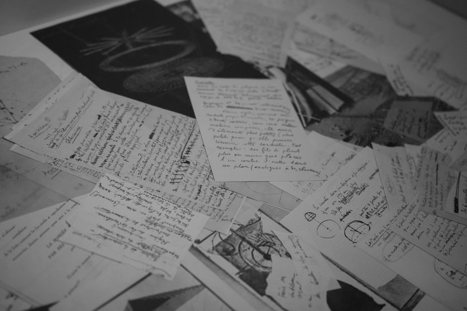 A collection of handwritten notes and sketches in black and white, scattered over a surface.