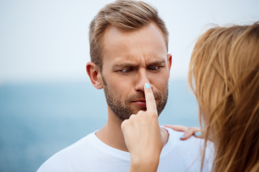 서양의 젊은 남녀가 서로 마주보고, 여성이 남성의 코를 누르고 있고 남성은 본인의 코 끝을 보며 우스깡스러운 표정일 짓고 있는 것을 찍은 사진