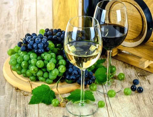 나무 쟁반에 청포도와 검은포도가 가득하고, 앞에는 화이트 와인과 레드와인이 담긴 유리잔이 있다.