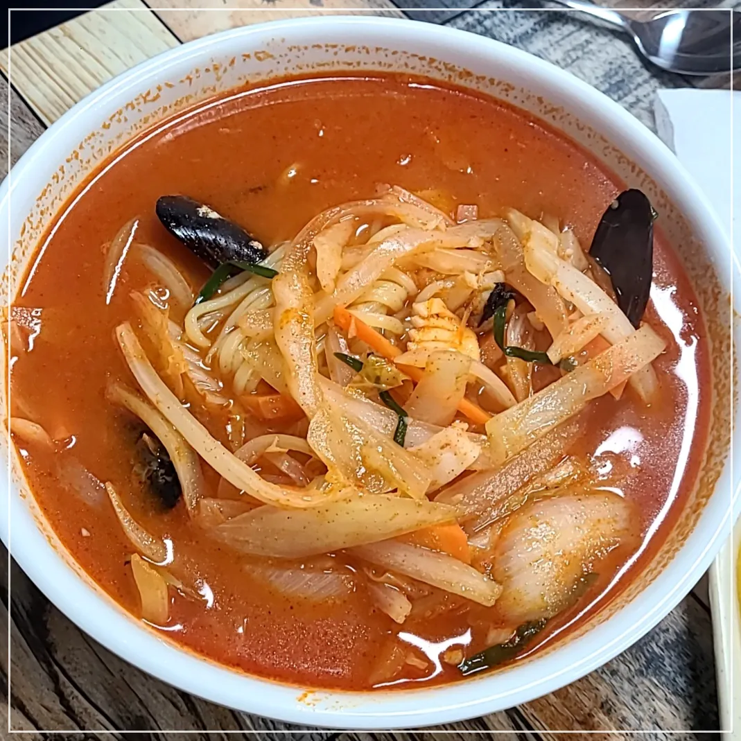 나무테이블 위 흰그릇에 수북히 쌓인 짬뽕이 담겨있음