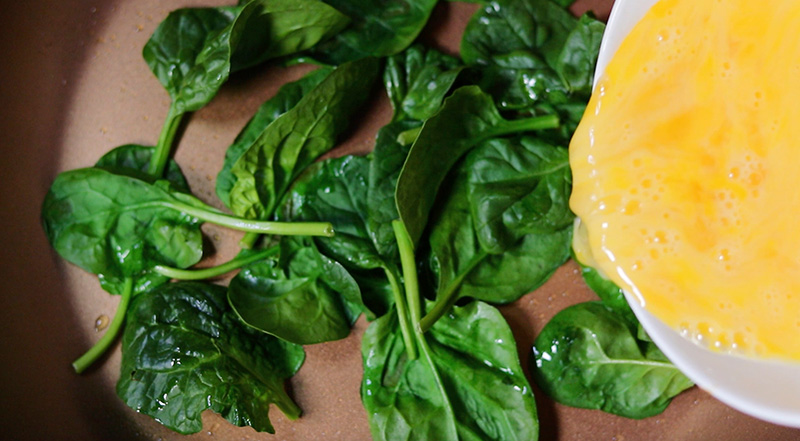 팬에 있는 시금치에 푼 달걀 붓기