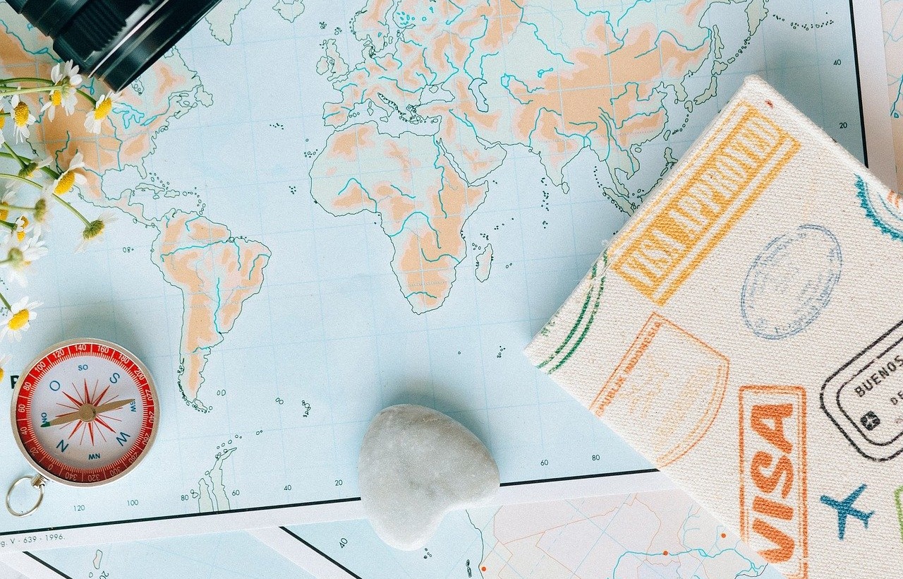 세계 지도 위에 여권 커버와 카메라, 그리고 나침반이 올려져 있는 사진