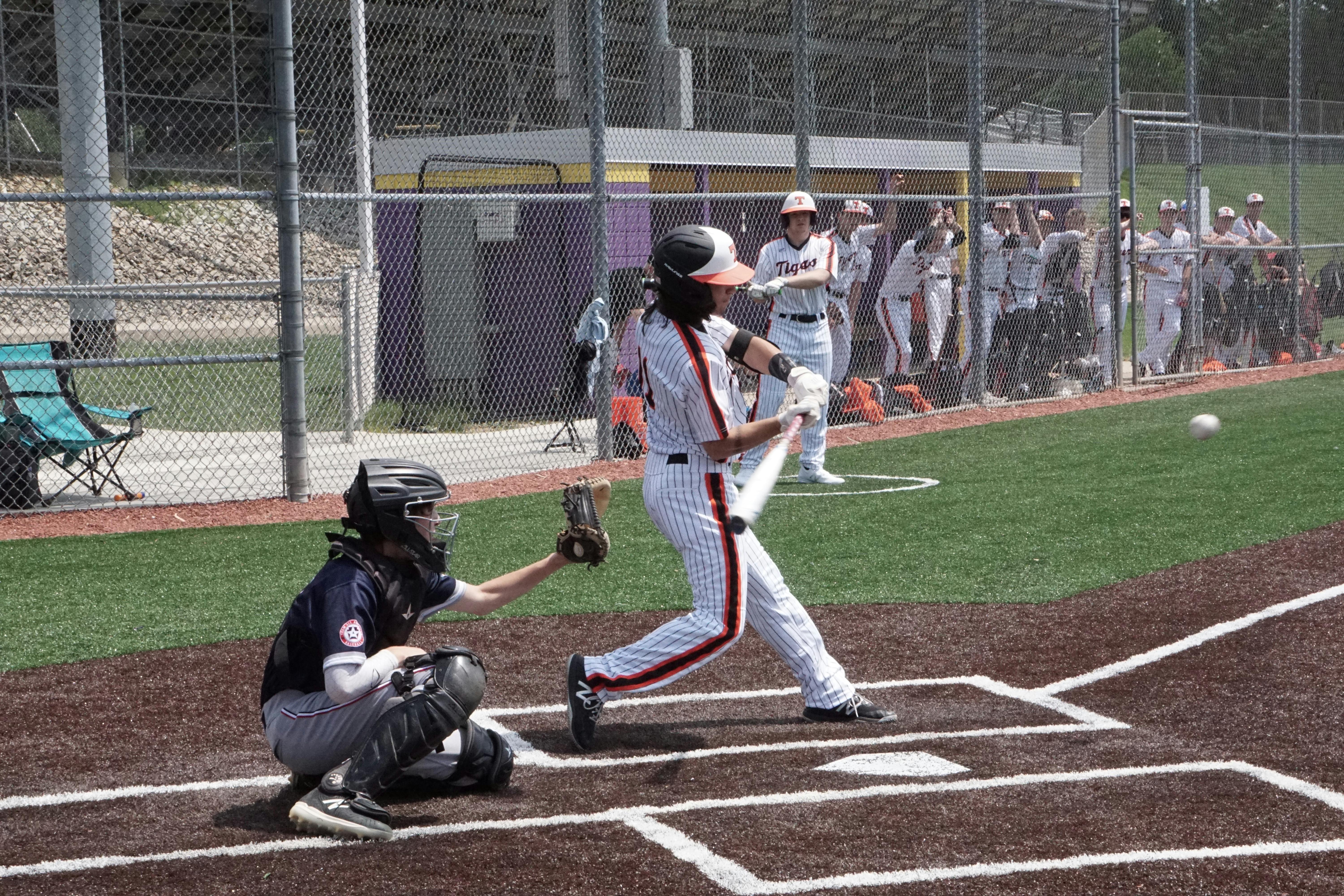 타석에 선 타자가 배트를 휘두르는 순간, 포수가 앉아 있고 야구공이 공중에 떠 있는 야외 야구장 경기 장면.