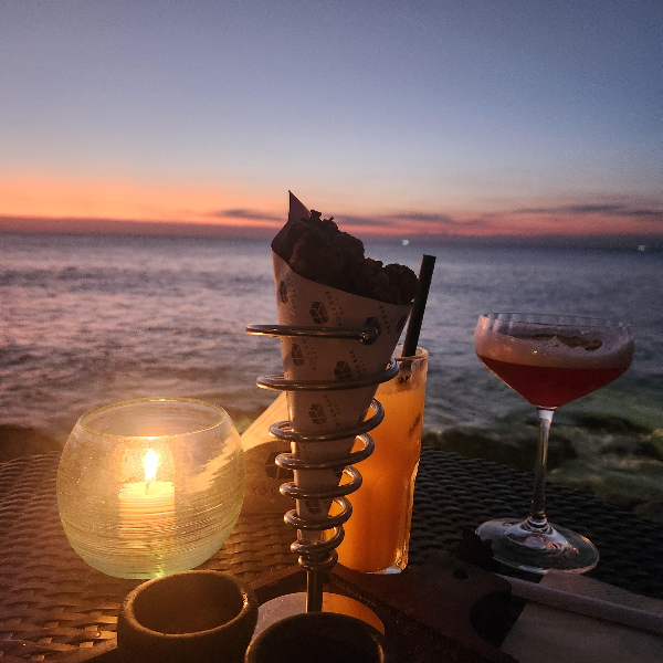 노을 지는 바다를 배경으로 칵테일 두 잔과 간식