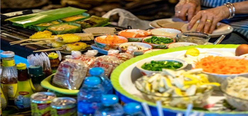 시장 음식점의 조리대 위에 다양한 식재료가 가지런히 놓여 있고, 한쪽에서는 요리사가 손으로 음식을 준비하고 있는 장면.