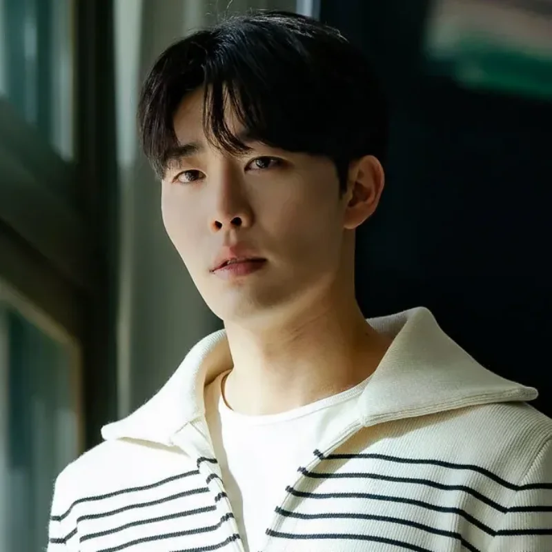 어느 창문이 있는 교실을 배경으로 크림색 옷에 단정한 머리를 하고 있는 국민사형투표의 이민수