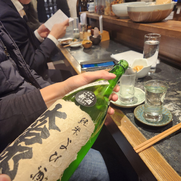 바형 테이블에 서빙 중인 직원. 큰 사케병으로 사케를 따르고 있다.