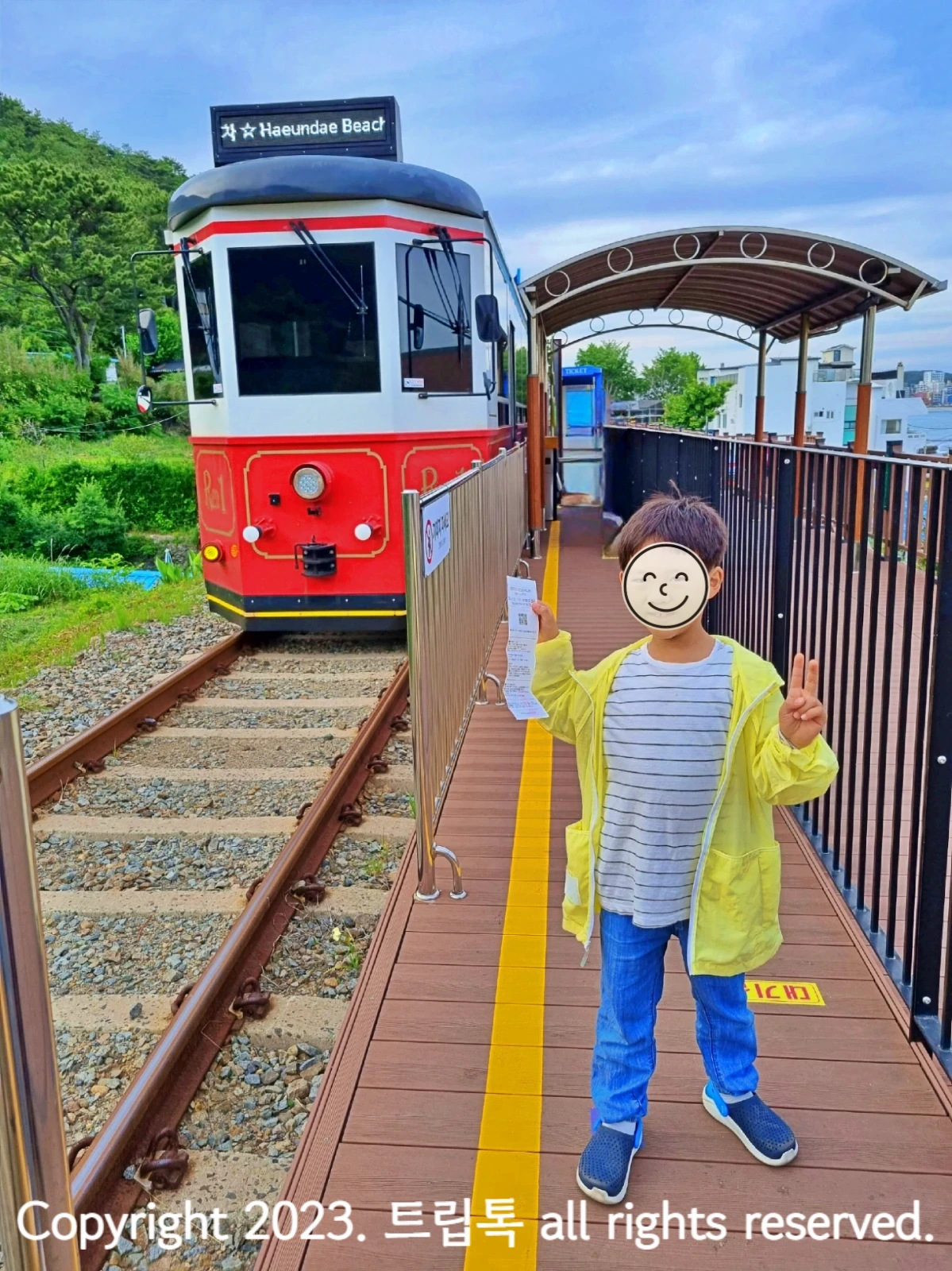 왼쪽에 빨간 열차가 선로를 따라 들어오로 오른쪽아 아이가 티켓을 들고 있다.