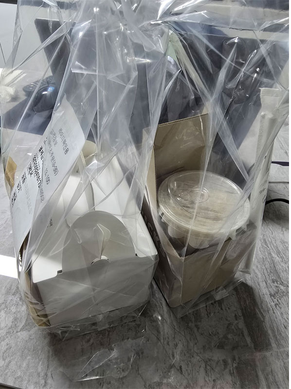 “스타벅스 배달로 도착한 커피와 디저트, 비닐 포장 안에 컵과 케이크 박스가 담겨 있는 장면.”