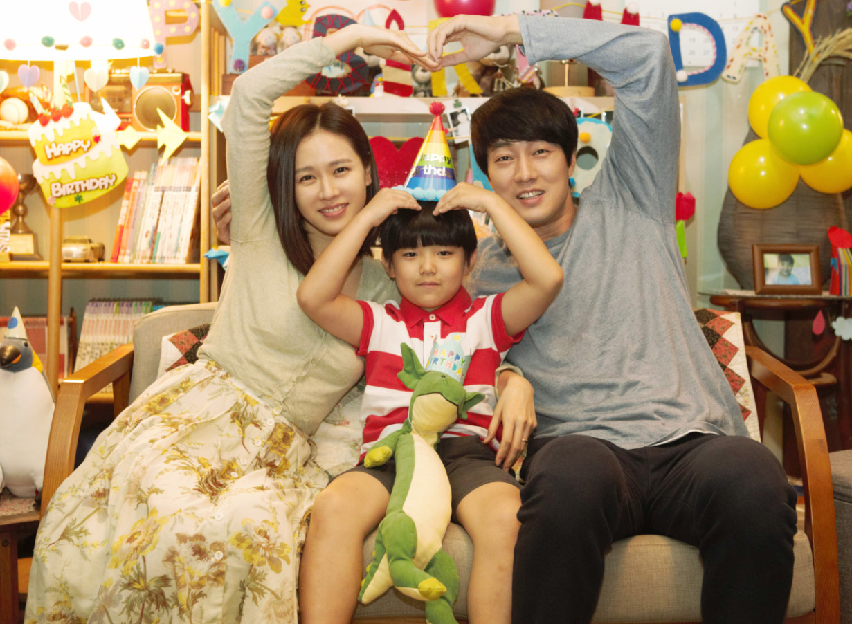 지호의 생일파티에서 수아와 우진이 지호 머리 위로 하트를 만들며 나란히 웃고 있는 가족 장면