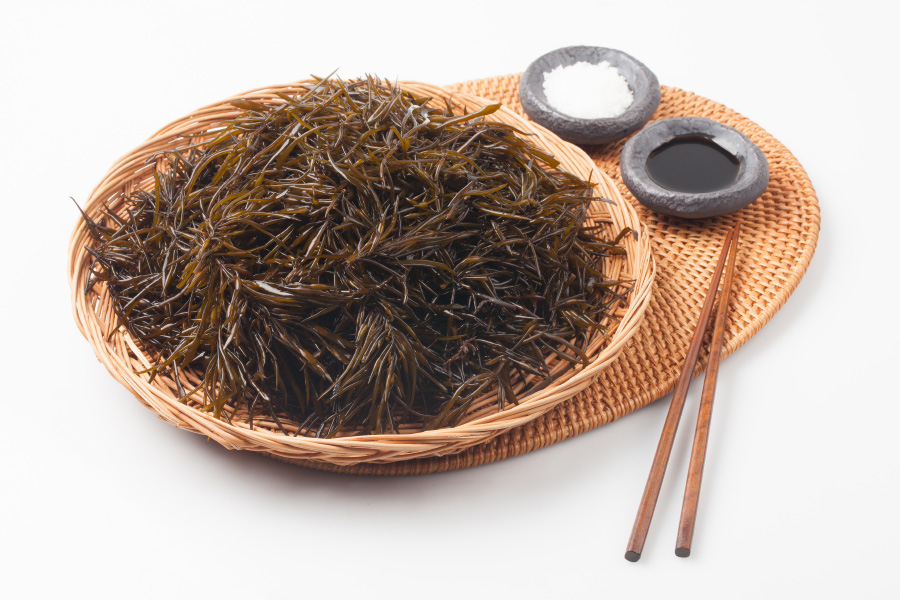 바다에서 채취를 한 톳을 깨끗하게 세척한 후에 하얀 바닥 위에 대나무로 만든 깔판을 깔고 그 위에 대나무 소쿠리에 가득 담아두고 그 옆에 간장과 소금을 담은 그릇과 나무젓가락을 두고 찍은 사진