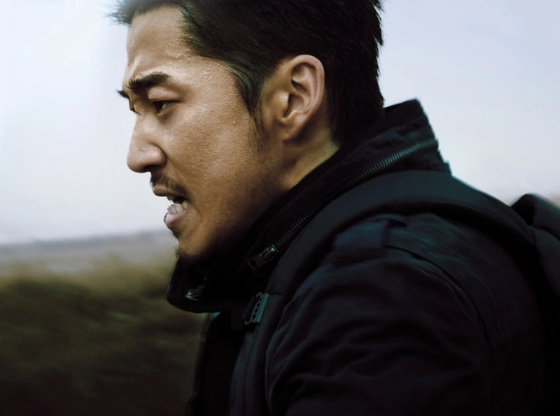 갈대밭을 배경으로 짧은 머리에 검은 점퍼를 입고 달리고 있는 영화 풍산개에서 풍산을 연기하는 배우 윤계상