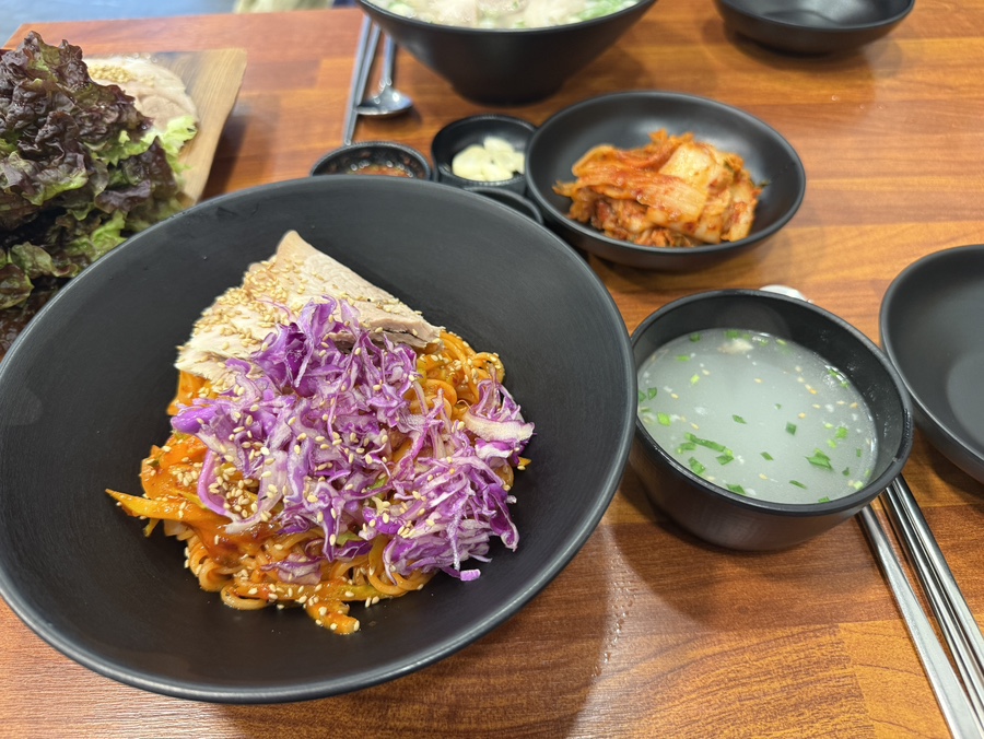 그릇에 담긴 비빔국수 사진. 붉은 양념과 면이 잘 섞여 있고 위에는 고명과 채소가 올려져 있어 풍미를 더한다.