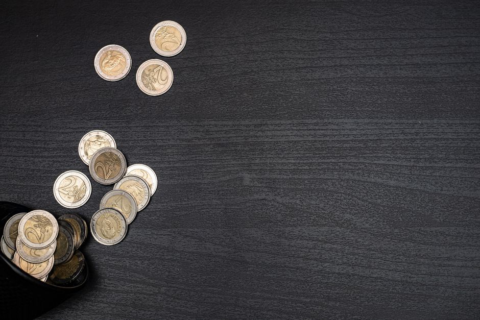 A collection of euro coins scattered on a dark textured surface, with space for text.