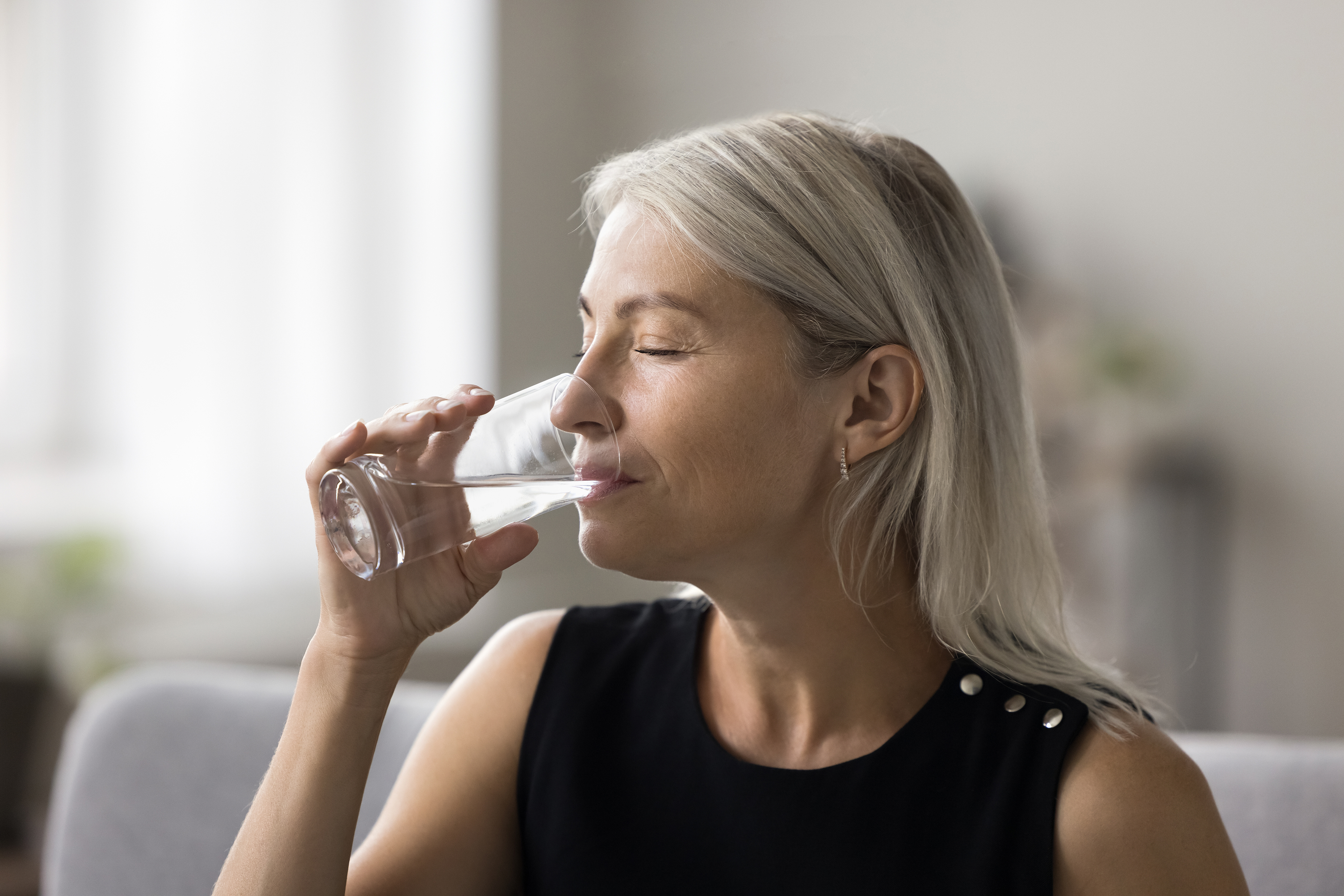 물 한 잔을 천천히 마시며 건강 관리를 실천하는 중년 여성 – 수분 섭취 루틴을 강조하는 장면