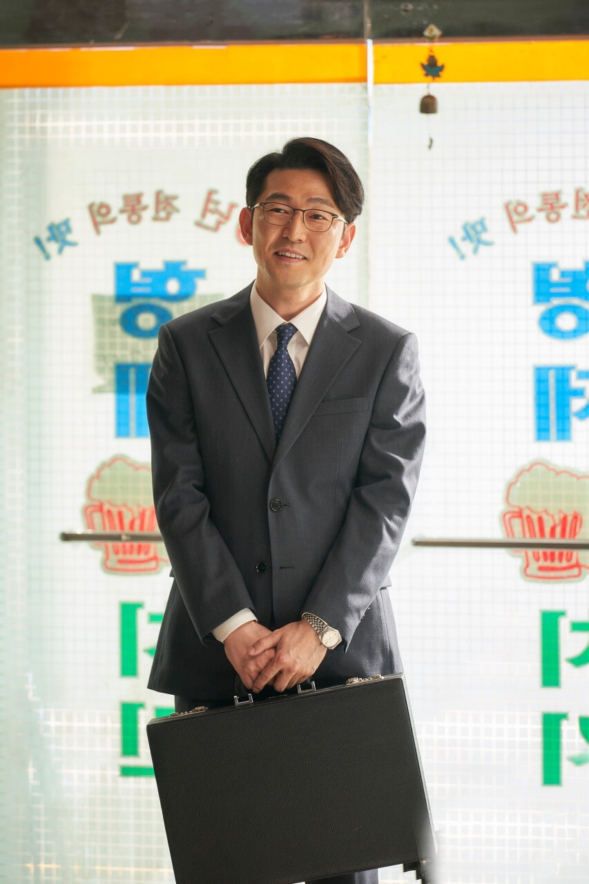 돈가방을 들고 공손히 서서 미소짓는 정실장