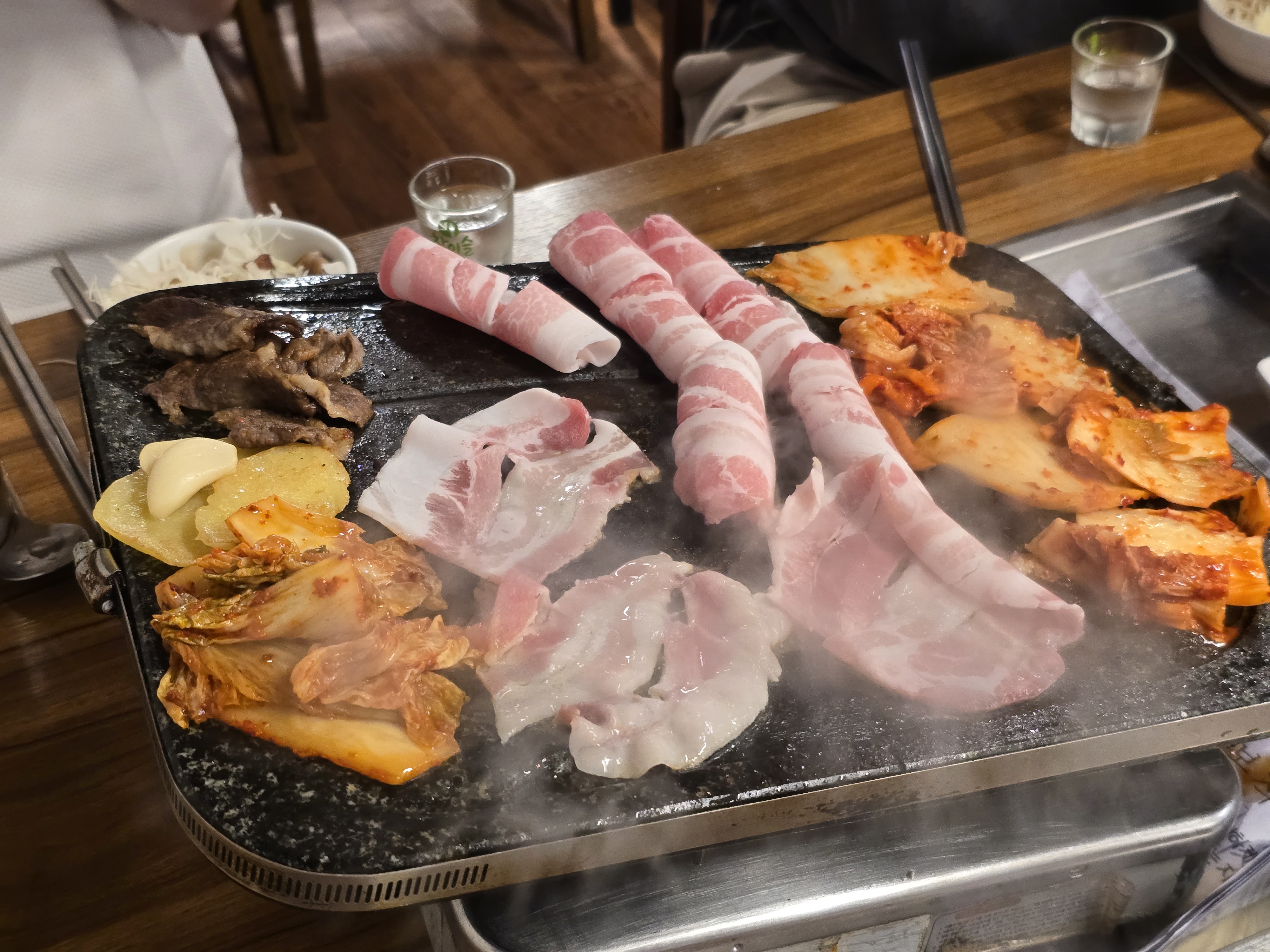 자연석 돌판 위에서 지글지글 익어가는 대패삼겹살과 차돌박이, 김치, 감자