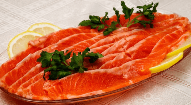 접시에 담긴 송어회로 붉은색 살이 싱싱해보인다. 송어 옆에는 레몬 조각들이 있다.