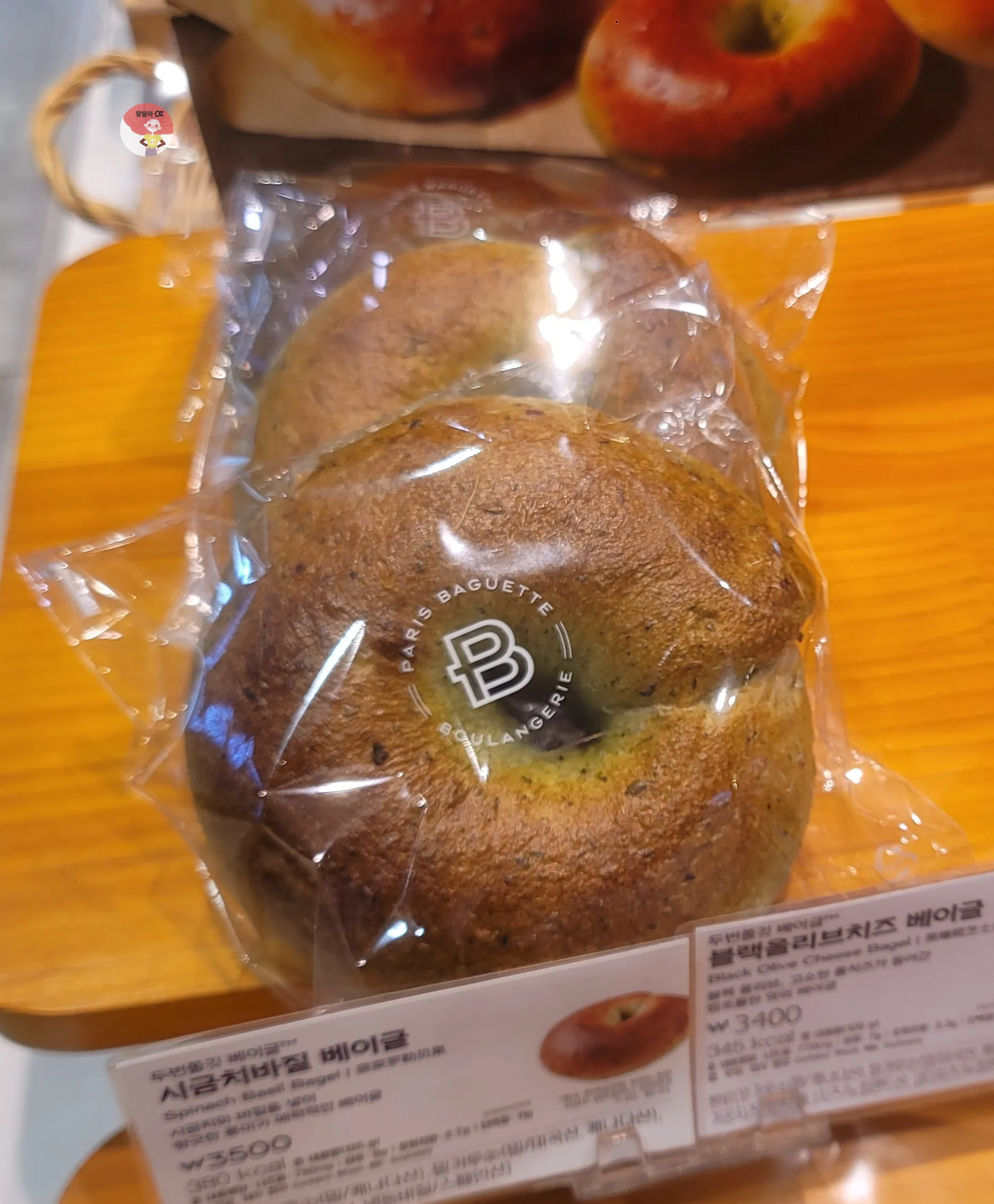 파리바게뜨 시금치바질 베이글 포장 이미지. 짙은 녹색빛 베이글이 투명 포장 안에 들어 있고, 제품 설명 라벨이 함께 보인다.