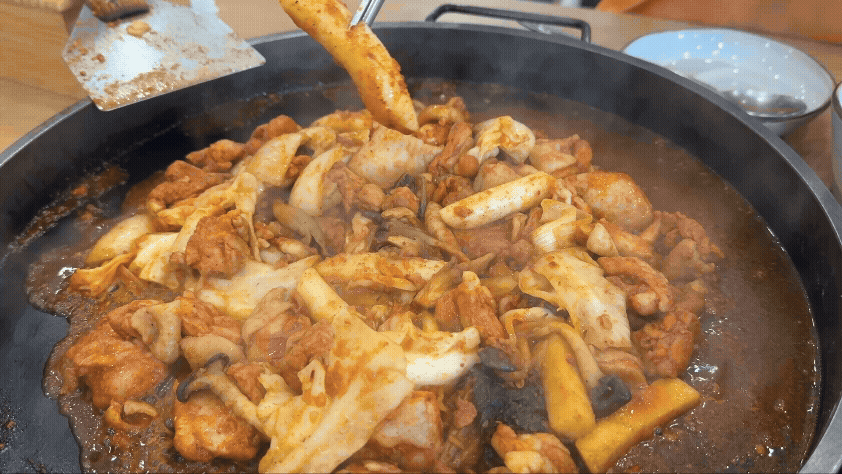 철판 위에서 갓 볶아지기 시작한 송정 닭갈비. 양념이 고루 스며든 닭고기와 떡, 채소가 자작한 국물 속에서 보글보글 익어가는 모습.