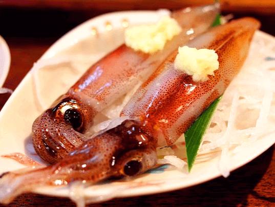 하얀 접시에 생 꼴뚜기 2마리가 나란히 있다. 꼴뚜기 아래에는 하얀 무채가 있고 꼴뚜기 눈동자는 크고 검정색이다.