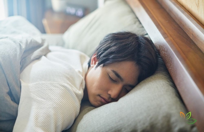 Young man sleeping peacefully in bed with white bedding and pillows near window with natural lighting VIA CANVA