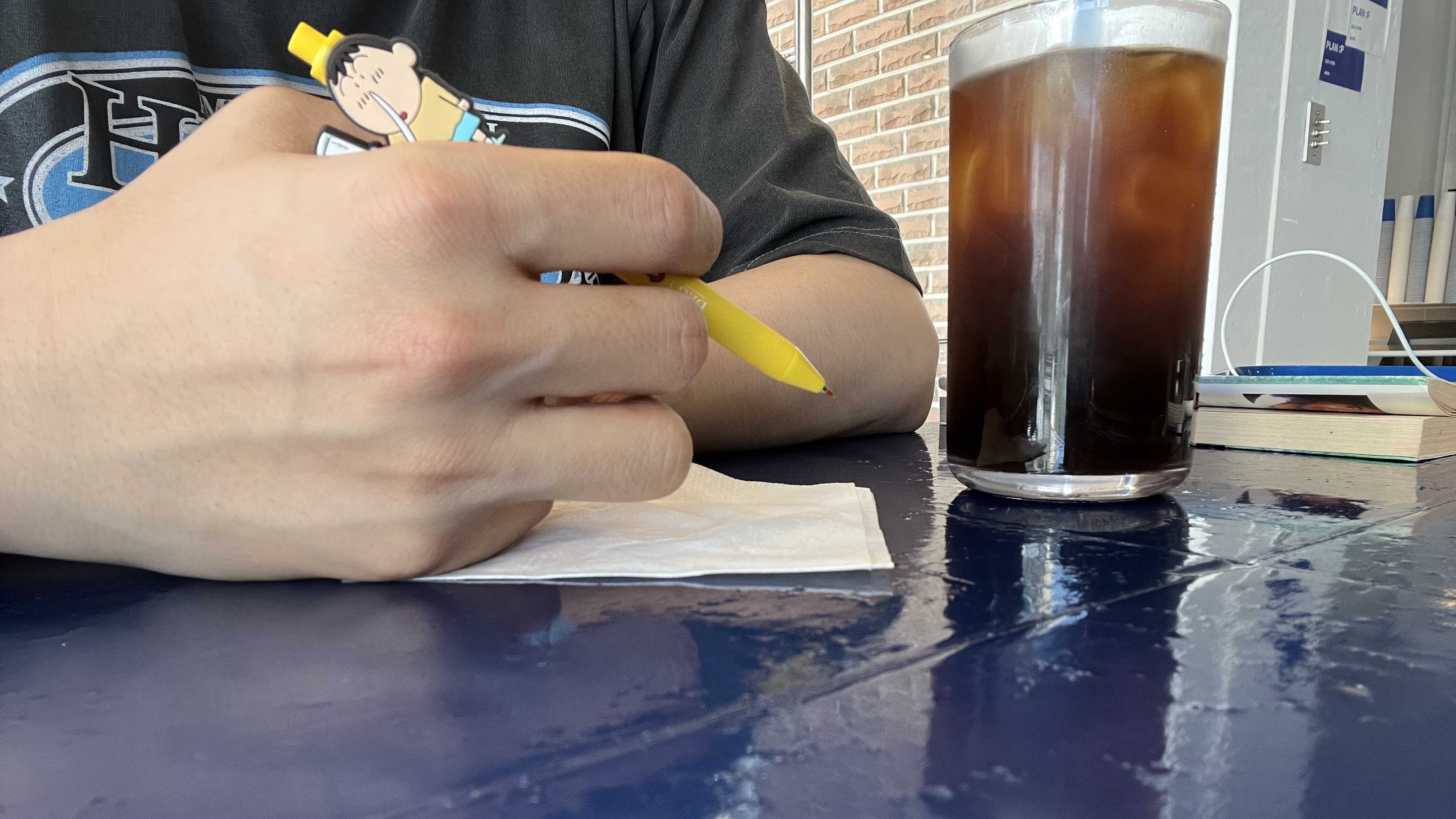 카페 테이블에서 펜을 들고 메모하는 손과 음료잔