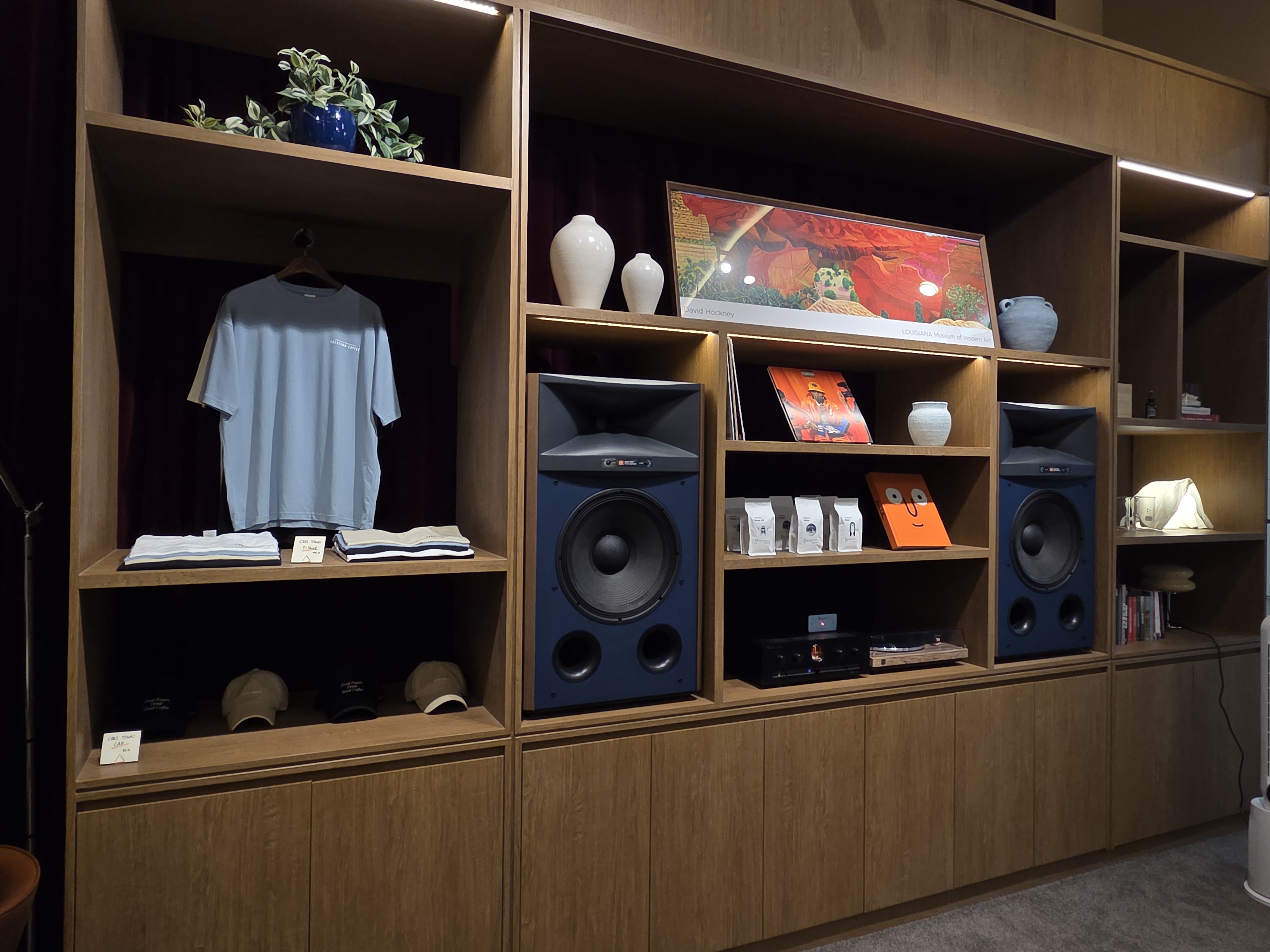 크레스타운 로고 티셔츠, 모자, 원두 패키지와 대형 스피커가 함께 전시된 공간