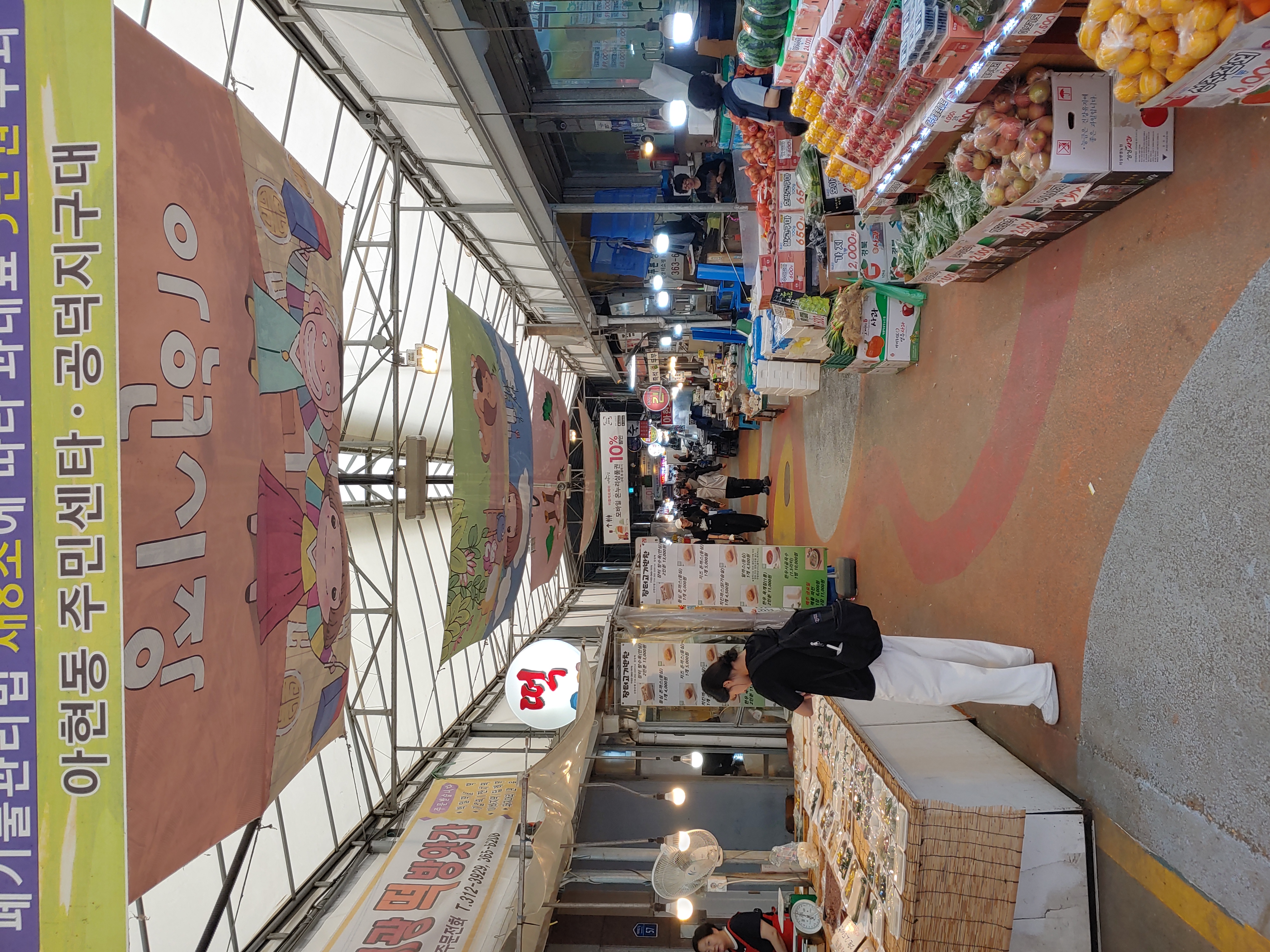 현대적인 조명과 천장 장식, 그리고 가지런하게 정돈된 상점들이 늘어선 아현시장 내부 풍경