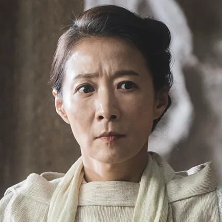 반백의 머리를 말아 올린 50대 여성이 흰 사제복을 입고 서 있는 아라문의 검 모명진 캐릭터