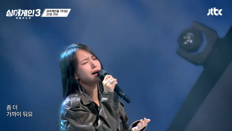 싱어게인3- 긴생머리에 오른손으로 마이크를 쥐고 눈을 감고슬프게 노래하는 27호 상반신