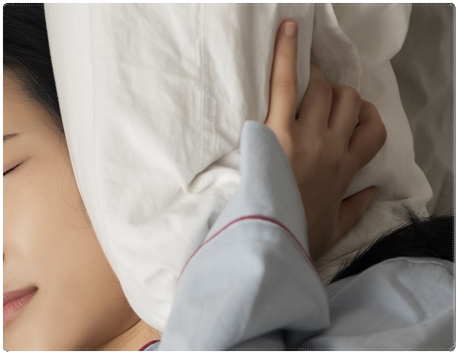 베개로 귀를 막은 채 다소 힘든 표정을 짓고 있는 여성의 모습