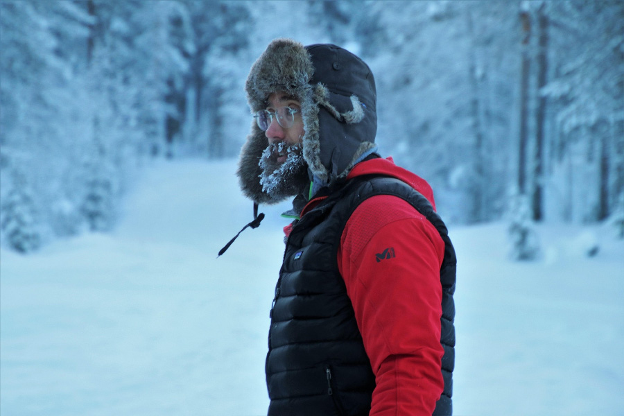 추운 산길에서 털모자와 동그란 안경을 쓰고 콧수염과 턱수염에 얼음이 얼은 남성의 옆모습을 찍은 사진