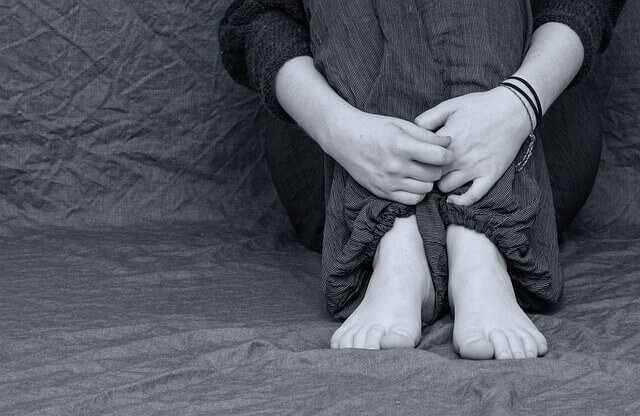 웅크리고 앉아 두 팔로 다리를 감싸고 있는 모습