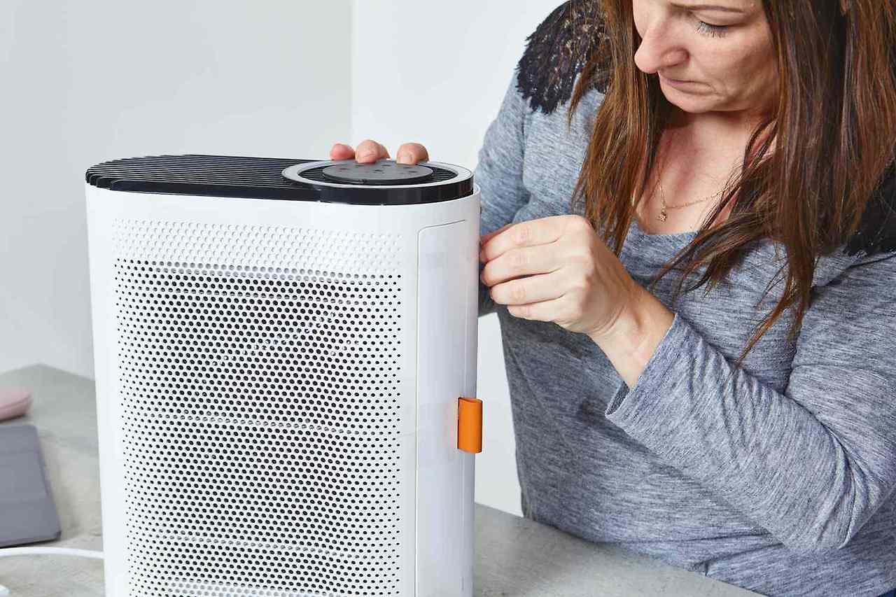 Person checking and cleaning the filters of an air purifier in a cozy home setting.