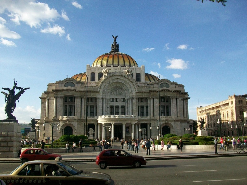 맑은 푸른 하늘 아래 웅장하게 서 있는 멕시코시티의 상징적인 예술궁전(Palacio de Bellas Artes) 건축물과 그 앞을 지나는 도심 전경