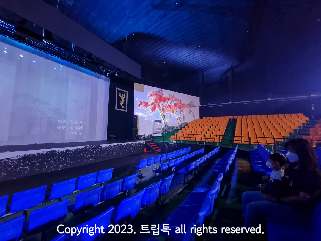 무대 오른쪽에 주황색 좌석과 벽화가 보인다