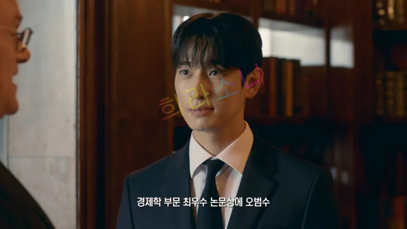 오범수가 검은색 정장과 흰색 셔츠&amp;#44; 검은색 넥타이를 착용하고 대화를 나누고 있다. 그는 단정한 머리 스타일을 하고 있으며&amp;#44; 정면을 바라보며 부드러운 미소를 띠고 있다. 자막에는 