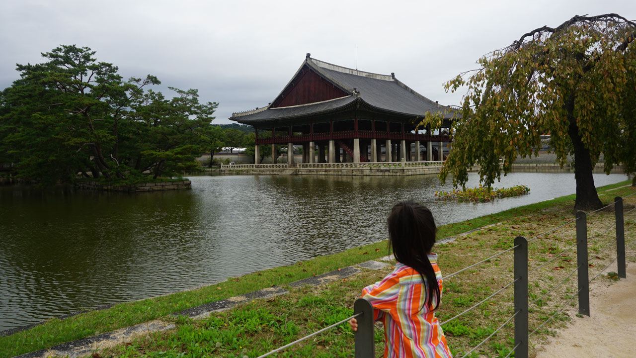 아이가 연못에 비친 누각을 바라고 있다.
