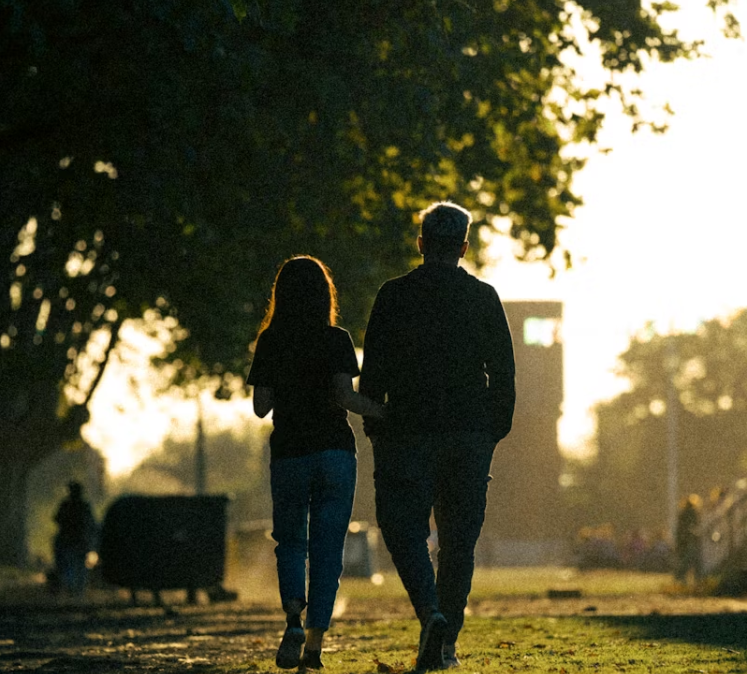 공원 산책길을 나란히 걷고 있는 두 사람의 뒷모습, 따뜻한 햇살이 비치는 저녁 풍경