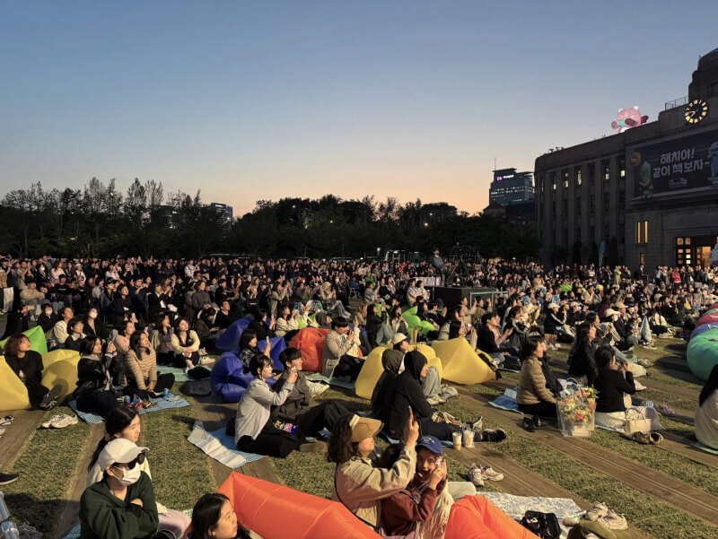 해 질 무렵 서울광장에서 수백 명의 관람객이 돗자리와 빈백 의자에 앉아 야외 공연을 감상 중인 장면