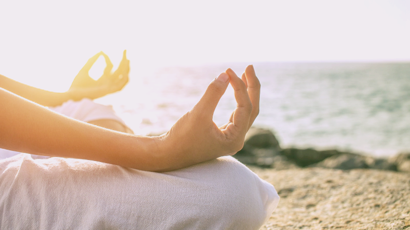 공황장애 증상 자가진단 치료 극복법에 관한 글의 이해를 돕기위한 이미지 : 바닷가 앞 모래사장 위에서 한 여성이 명상을 하고 있다.