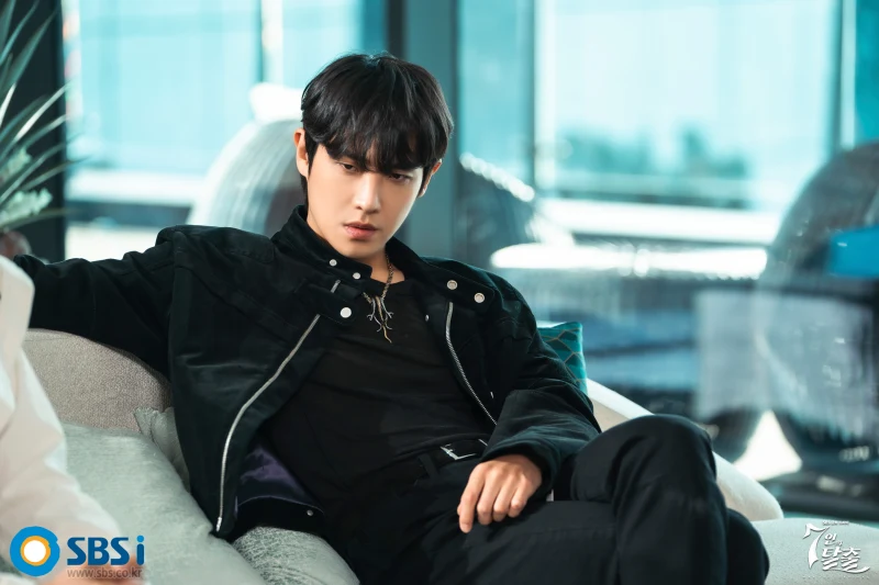 어느 실내의 고급 쇼파에 검은 자켓과 바지를 입고 앉아 있는 드라마 7인의 탈출의 민도혁 캐릭터