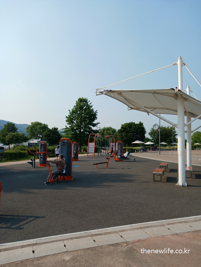 outdoor leg press machine at riverside fitness zone, sunny clear sky/맑은 날 강변 야외 운동기구 구역에서 하체 근력운동 기구를 이용하는 모습