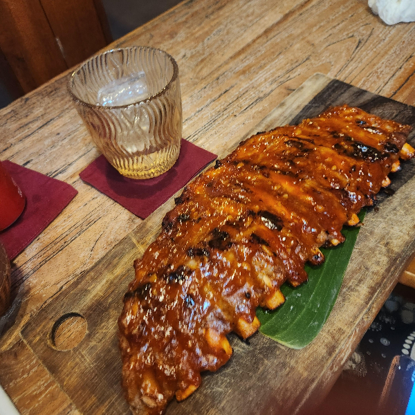 커다란 폭립과 컵이 보인다. 폭립은 도마 위에 잎을 깔고 그 위에 올려져있다.